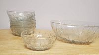 Six small glass bowls and two large glass bowls arranged on a wooden surface showing their clear glass and decorative cut pattern.