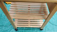 Close-up image of the wooden slatted shelves and wheels of the kitchen trolley