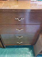 Front view of mid-century modern tallboy with four drawers and brass handles showing wood finish and condition.