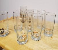 Nine clear glass tumblers with gold torch and Olympic rings design on wooden surface