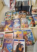 Photo showing Disney VHS tapes laid out including Beauty and the Beast, Cinderella, Snow White, Tarzan, Lion King, and others along with several DVDs and TV series boxes.