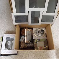 Top view of a cardboard box containing multiple picture frames of various styles and sizes including white collage frame and several smaller frames inside.