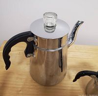 Close-up of metal coffee/tea carafe with black handle and glass knob on lid