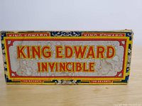 Top of King Edward Invincible cigar box with colorful branding and decorative borders.