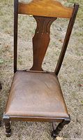 Single wooden chair with carved wooden back and brown leather seat, turned front legs, visible vintage wear.