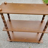 Front angle view of the three-tier wooden shelf showing its overall design and condition on an outdoor surface.