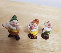 Front view of three Snow White dwarfs figurines; characters are Happy, Dopey, and Bashful in colorful ceramic with glossy finish.