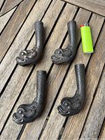 Four dark cast iron furniture feet shaped like dolphin heads with scaled tails. They are resting on a wooden slatted surface next to a green lighter for scale reference.