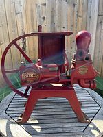Side view of the red cast iron pump with visible Durol Pump Mfg Co emblem and large flywheel on a wooden table outdoors.