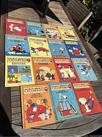 15 paperback Charlie Brown's Encyclopedia children's books outdoors on table, colorful covers with characters and text, minor wear visible
