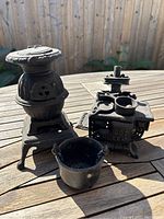 Three cast iron stove salesman samples on wooden table under sunlight showing details of the wood stove, cook stove, and pot.