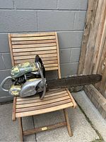 Side view of a vintage Pioneer chainsaw sitting on a wooden chair, showing the cutting bar length and handle.