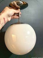 Photo showing the white glass spherical globe pendant light with polished metal mounting and rod, held in hand to show size and details.