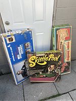 Three vintage board games leaning against a wall outside: Over The Top Hockey, Aurora Skittle Pool, and Snap Bowling.