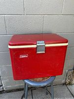Red vintage Coleman cooler closed, showing overall exterior, latch and logo on front.