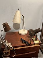 Three vintage desk lamps on a wooden surface against a gray wall