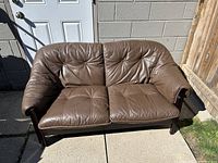 Front view of brown leather loveseat showing tufted seat and back cushions and wood frame