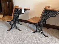 Side view of two antique wooden school desks showing cast iron sides with intricate cut-out patterns and wooden seats attached.