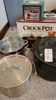 Original Crock Pot box and Rival Potpourri Crock Pot box with stainless steel and black stock pots and canning pot in front