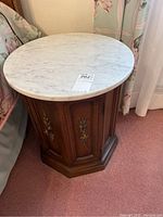 Side view of one nightstand showing white marble top, octagonal wooden base, and door with metal hardware.