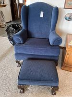 Front view of a navy blue wing chair with matching footstool showing claw feet and seat cushions.