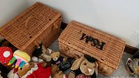 Two large rectangular wicker baskets arranged next to each other on floor with assorted stuffed animals visible around and inside them.