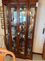 Front view of tall wooden curio cabinet with glass paneled doors showing multiple shelves with decorative items inside.