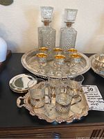 Close-up of cut glass decanters and six silver plated mini goblets on large tray highlighting glass patterns and gold interiors.