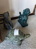 Three decorative figurines shown together on carpet: a cherub, a green dragon, and a turtle.