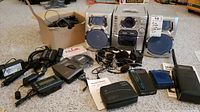 Wide view of all electronics included in lot, showing disc player, scanner, portable phones, chargers, and other devices arranged on floor.