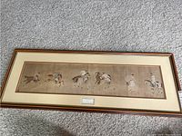 Framed artwork showing polo players on horseback laid on carpet.