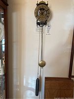 Full view of the Tempest Fugit German wall clock mounted on wall with pendulum and weight chains visible.