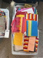 Top view of a plastic bin filled with assorted colorful tissue paper sheets in various solid colors and stripes.