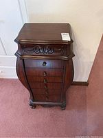 Front view of wooden jewelry chest showing carved decorative details and multiple drawers.