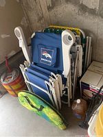 Multiple folded lawn chairs stacked upright including a Denver Broncos branded chair, adjacent to an old red fire extinguisher and box.
