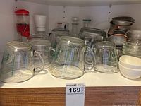 Front view of glass measuring cups arranged on shelf, showing measurement markings and varying sizes