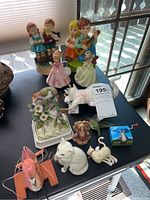 Photo of all 12 assorted decorative figurines and musical dolls on a table, in natural light near window
