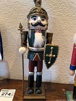 Close-up image of green soldier nutcracker holding spear and shield with gold detailing.