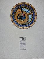 Replica Prague astronomical clock mounted on white textured wall with auction tag below it.