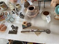 Photo showing various small pottery pieces, ceramic figurines including a person statue with blue top, decorative candle holders, glass box, and a WELCOME horse plaque.