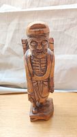 Front view of hand-carved wooden man figurine wearing a hat and carrying a basket on his back.
