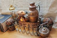 Full lot view showing all items from a slight angle on wood surface with backdrop, including glassware, metal items, and feather balls.