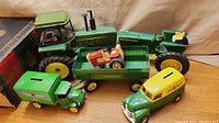 Group photo showing the large John Deere tractors, grain wagon trailer with small red toy tractor inside, John Deere green delivery truck and yellow-green ERTL panel van coin bank.
