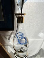 Full view of the hand painted glass decanter showing overall shape, stopper, and painted blue flowers with gold trim