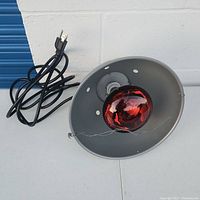 Heat lamp reflector with red bulb installed and black power cord with plug adapter visible.