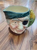 Front view of ceramic Long John pirate Toby mug with green hat, eye patch, and yellow-green parrot handle.