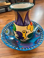 Photo of the Mexican pottery vase placed inside the blue decorative bowl, showing colorful bird and floral motifs on the vase with a dark green rim.