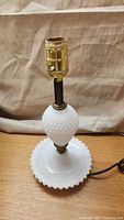 Full view of the small milk glass hobnail lamp showing circular base with scalloped edge, hobnail midsection, brass light bulb socket with knob switch, and attached electric cord.