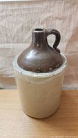 Front view of vintage moonshine jug showing beige stoneware body and dark brown glazed top with handle