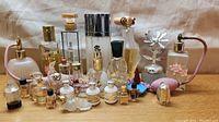 Overall front view showing all perfume and tester bottles arranged on a wooden surface with beige fabric background, including larger brand bottles and smaller testers.